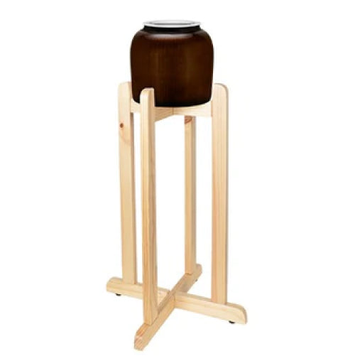 A brown ceramic jar with a white lid is placed on a tall, light wooden stand with four legs and a crossbar at the base.