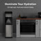 A Bottom Load Water Dispenser - Model 430 with a stainless steel finish and LED night light stands next to a kitchen counter and oven in a modern kitchen. Combining style and convenience, this hot and cold water dispenser features an illuminated indicator display, making it the ideal addition to any home. Text above reads, Illuminate Your Hydration. LED Night Light | Illuminated Indicator Display.