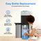 A woman kneels to easily place a large water bottle into the bottom compartment of the Stainless Steel Bottom Load Water Dispenser - 520. The text highlights hassle-free, easy bottle replacement that eliminates heavy lifting, fitting both 3- and 5-gallon bottles. This tri-temperature water cooler also features self-cleaning UV technology for added convenience and enhanced hygiene.