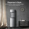 A Self-Cleaning Stainless Steel Bottom Load Water Dispenser - Moderna 730 stands beside a curtain and a dark cabinet adorned with books and a plant, set in a modern room with a gray wall and round clock. Text above highlights its stylish, premium design, tri-temperature dispensing, and advanced self-cleaning UV technology.