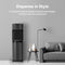 A modern living room featuring a gray sofa, a floor lamp, a side table with books and a plant, and the Black Stainless Ultrafiltration Bottleless Water Dispenser - 520 offering advanced water filtration—all set against a light gray wall with promotional text displayed above.