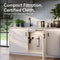 The 11″ Premium Under Sink Filter PFAS-Reduction System mounted on a white kitchen cabinet door, shown in a bright modern kitchen with the text 'Compact Filtration. Certified Clean.
