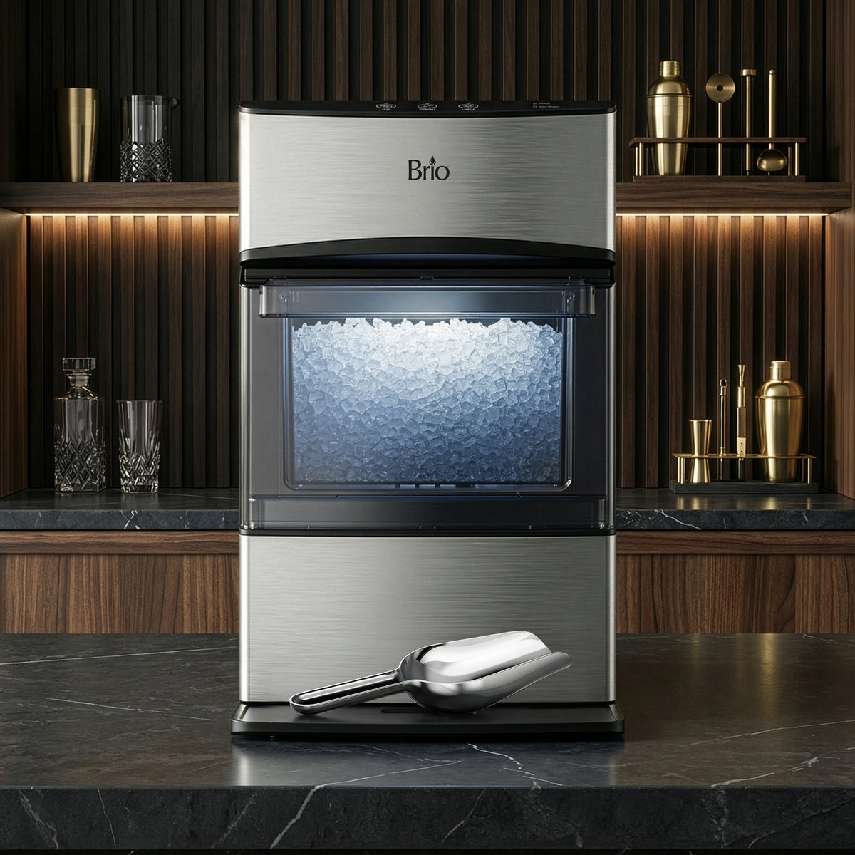 The Countertop Nugget Ice Maker - 740i, crafted from stainless steel, sits on a dark marble countertop overflowing with fresh nugget ice. A metal ice scoop rests in front of the machine. Behind it, wood paneling, shelves stocked with glassware, and golden bar accessories complete the background.