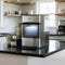 The Countertop Nugget Ice Maker - 740i sits on a modern kitchen counter with mugs stacked nearby, potted plants, and shelves with dishes in the background. The ice maker's self-cleaning storage bin is illuminated.