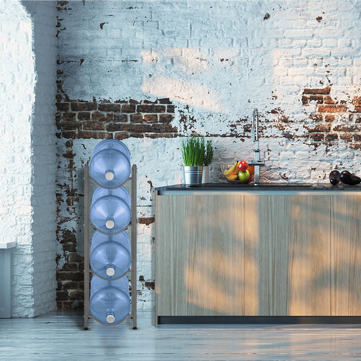 A modern kitchen features a rustic white and exposed brick wall, a wooden countertop with a sink, fruit bowl, potted plant, and the Single Column 4-Bottle Storage Rack - Gray holding four large blue water jugs.