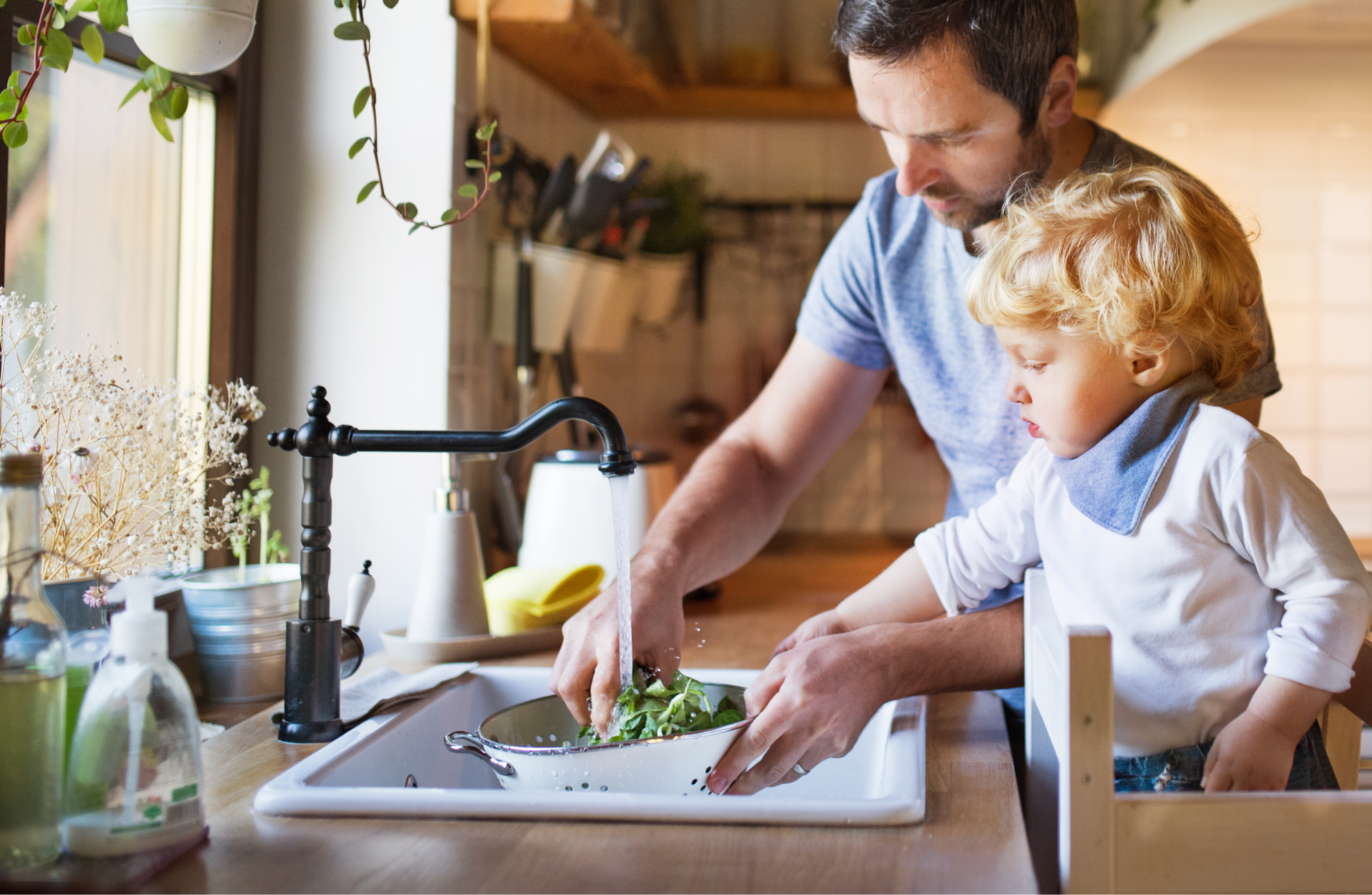 A father with a toddler boy washing vegetables in a kitchen sink