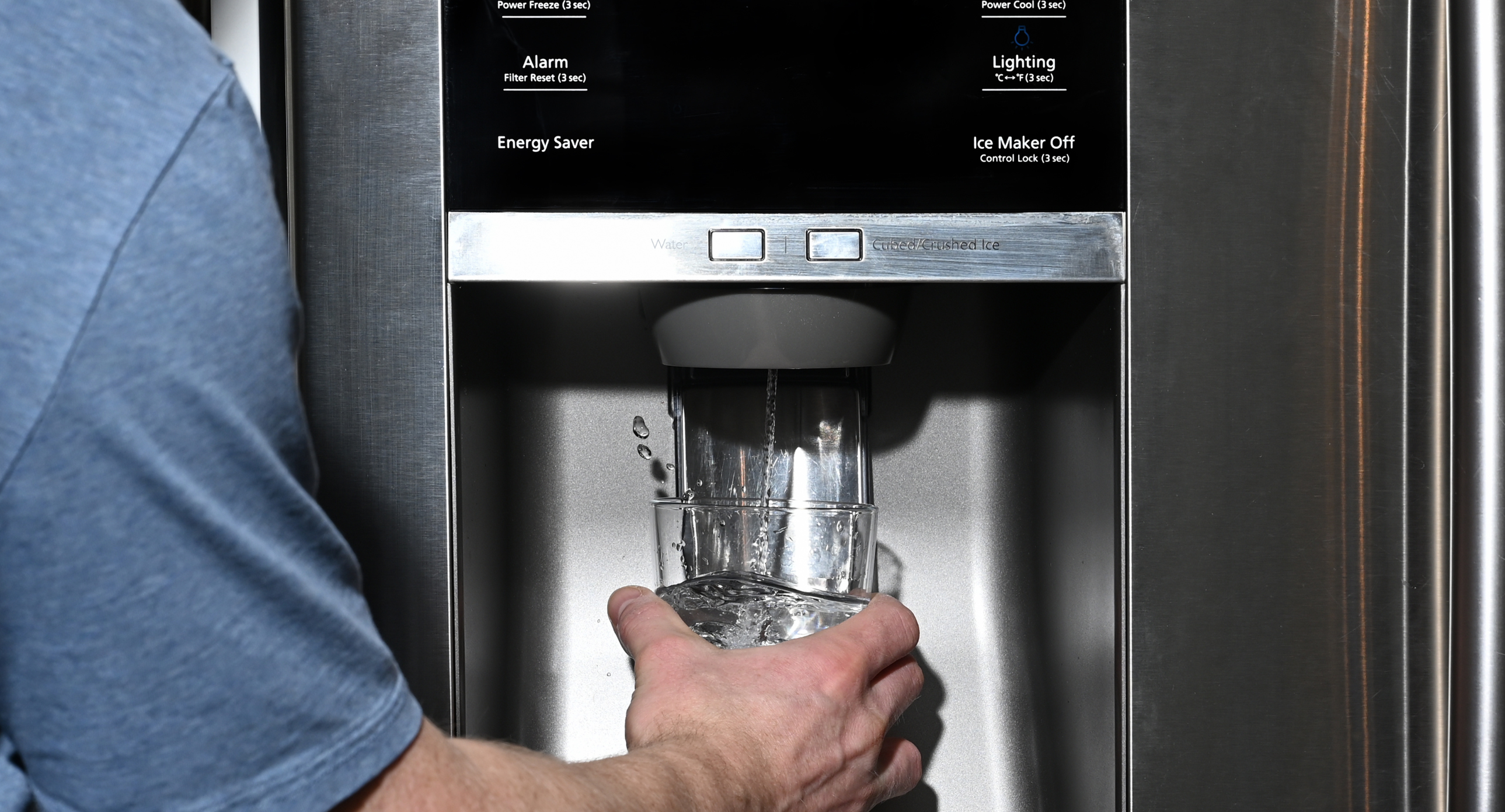 A man filling a glass with water splashing out of dispenser of home fridge