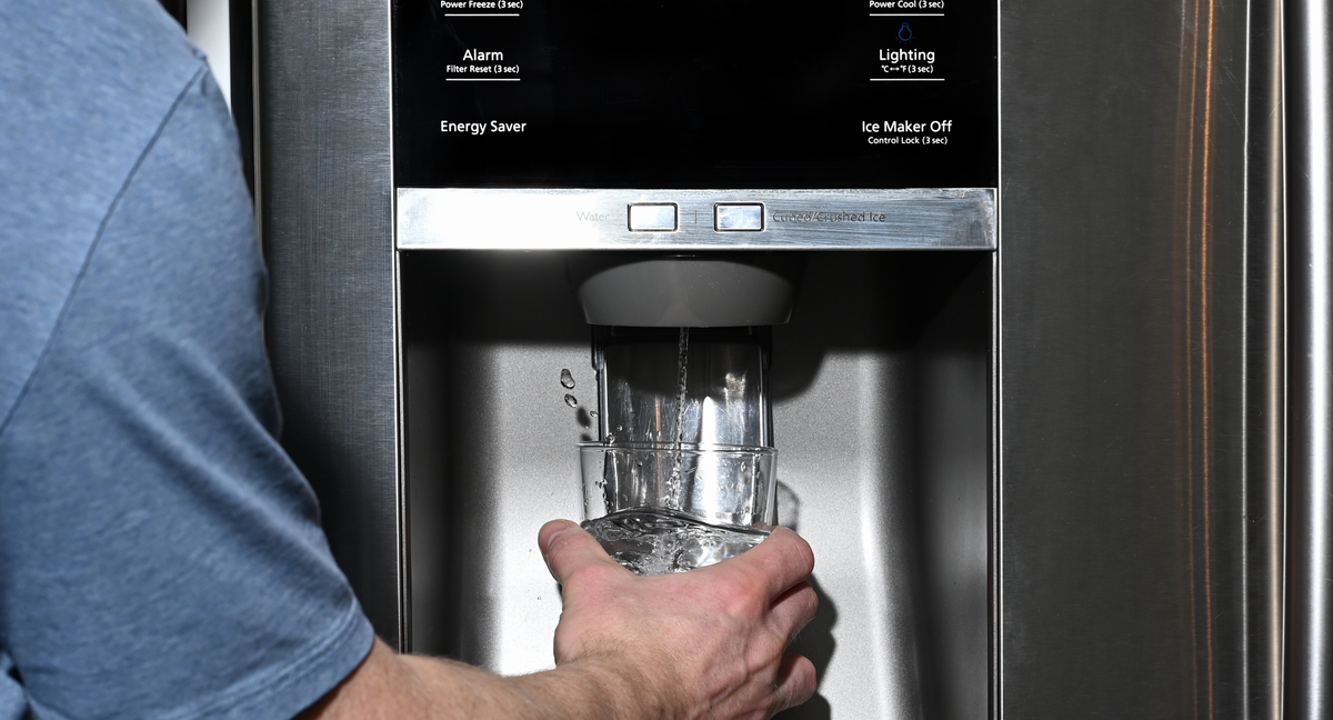 A man filling a glass with water splashing out of dispenser of home fridge