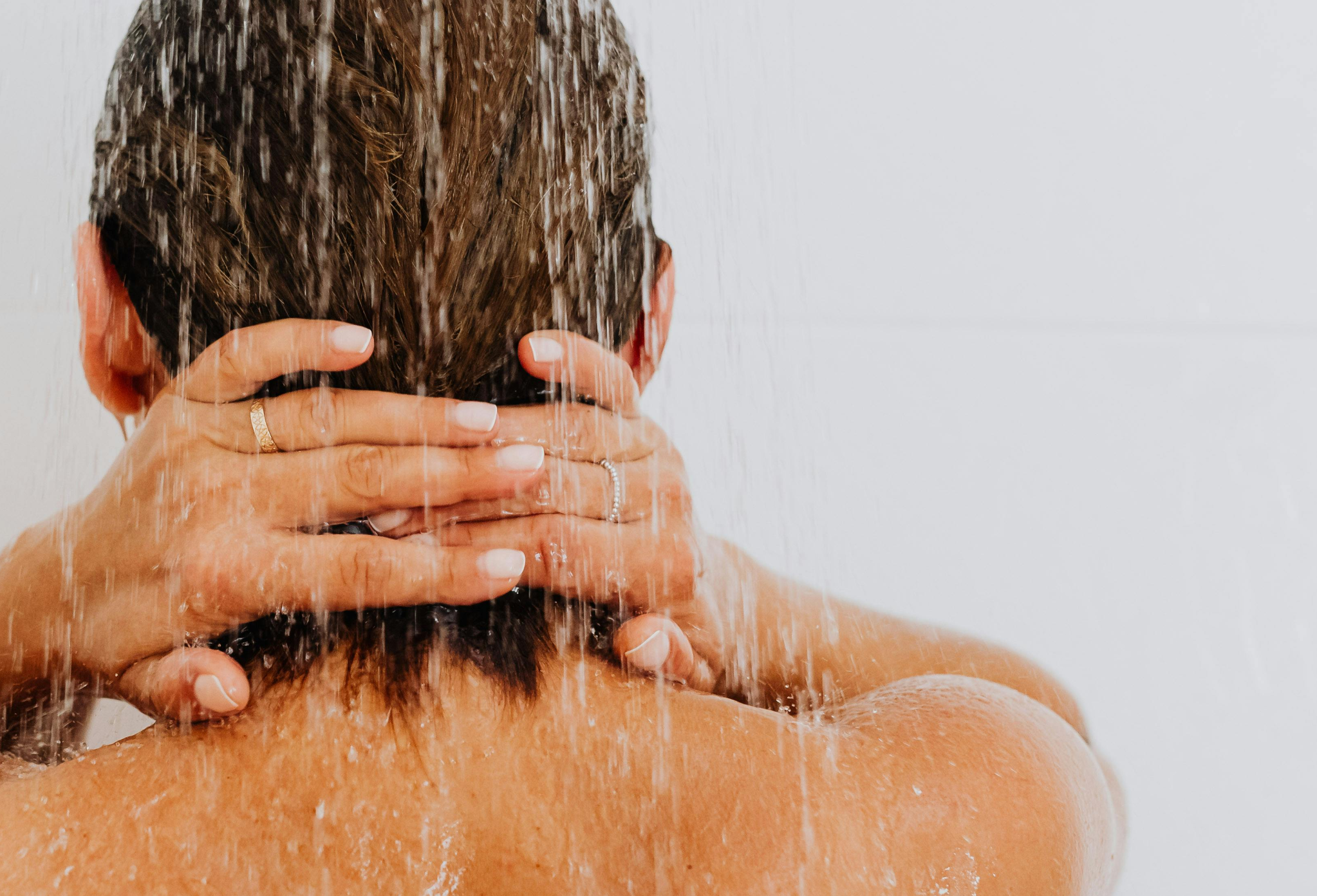 back of a woman's head in the shower with her hands clasped behind her neck 