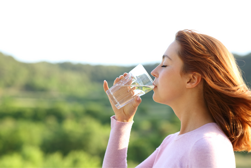 A woman drinking a glass of fresh filtered water out in nature