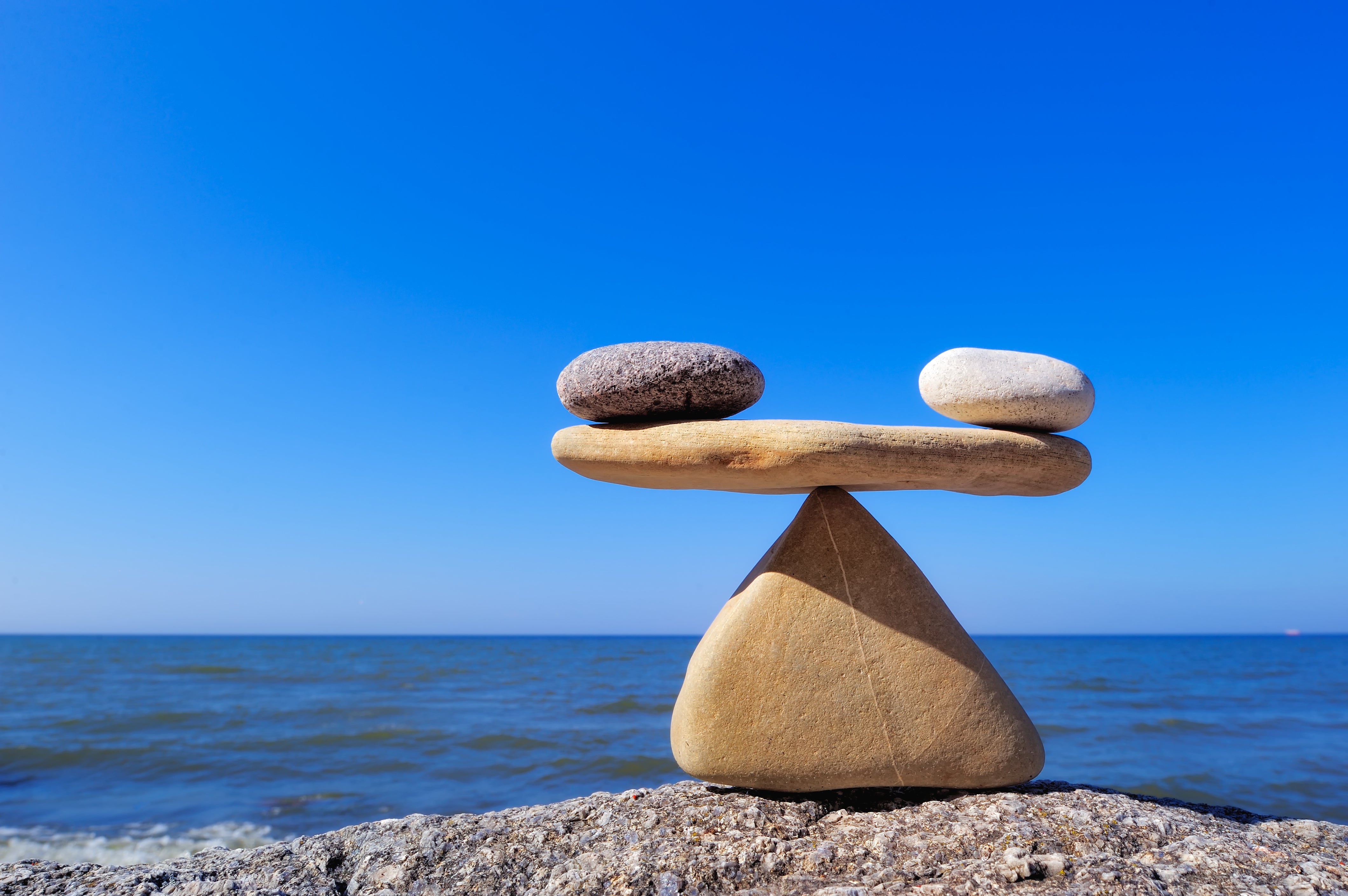 A white stone and black stone sitting on a flat stone which, in turn, is balanced atop a stone shaped like a pyramid.