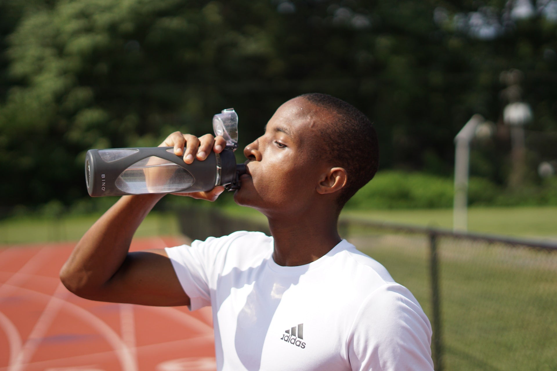 sportsman drinking from a resusable water bottle on an athletics track