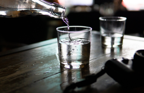 Water being poured from a glass bottle into a short glass