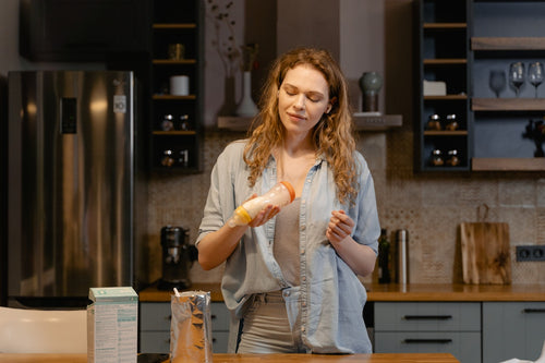 woman standing at kitchen worktop preparing a bottle of baby formula