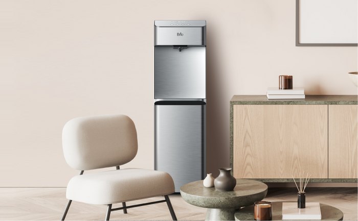 Brio 730 stainless steel bottom-loading water cooler in a modern living room with neutral tones, a minimalist chair, and a wooden console.