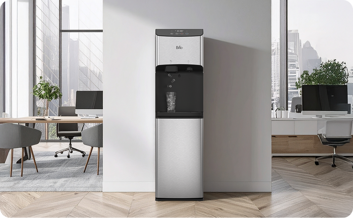 Brio 520 stainless steel ice & water cooler dispenser placed in a modern office with bright natural light, desks, and plants visible in the background.