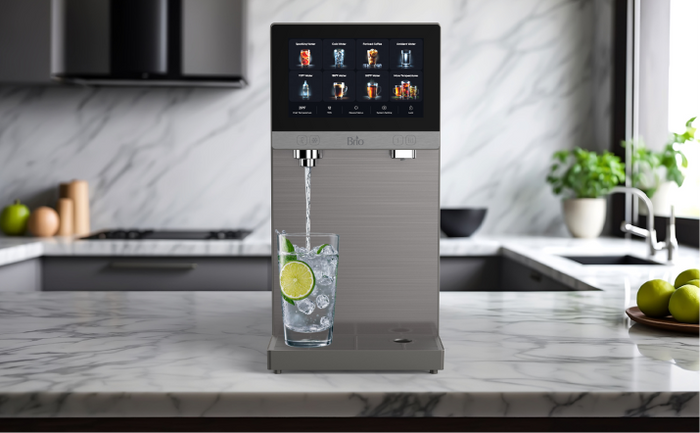 Brio Q60 reverse osmosis countertop sparkling water dispenser with a touchscreen display, dispensing purified water with lime slices in a modern marble kitchen.