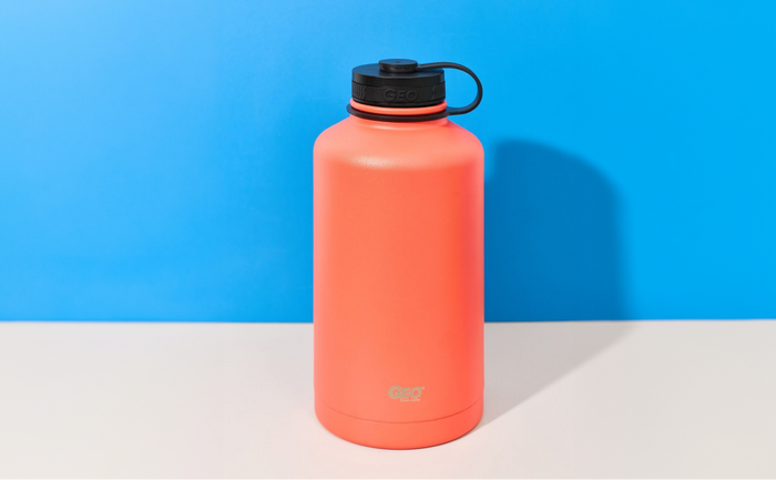 Bright coral GEO stainless steel sports water bottle with black screw-on cap on a blue and white background.