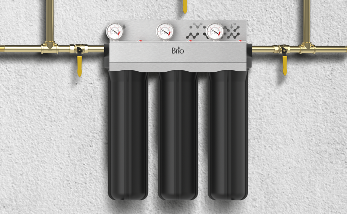 Brio 3-stage whole house water filtration system with three black filter housings and pressure gauges, mounted on a wall with brass piping.