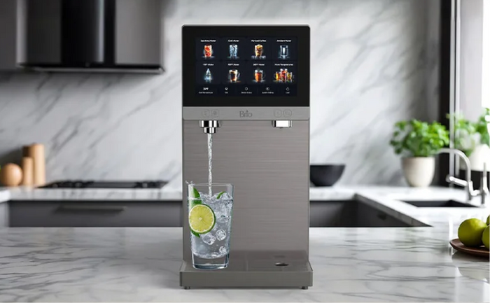Brio refillable countertop water dispenser with digital touchscreen, dispensing sparkling water with lime in a modern marble kitchen.