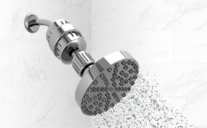 Brio chrome shower filter attached to a rainfall showerhead, releasing clean filtered water against white marble tiles.