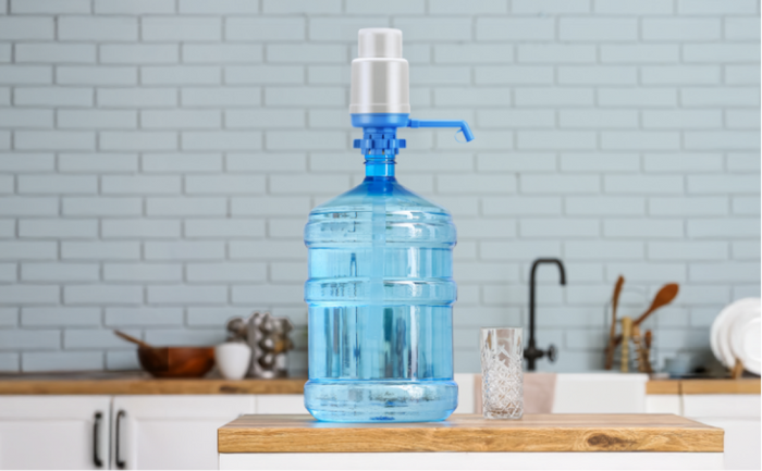 Brio manual water bottle pump attached to a 5-gallon water bottle on a kitchen counter beside a glass.