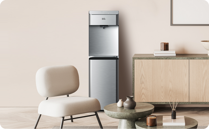 Brio 730 Series stainless steel water cooler dispenser displayed in a minimalist home setting with neutral tones, a chair, and decorative table pieces.