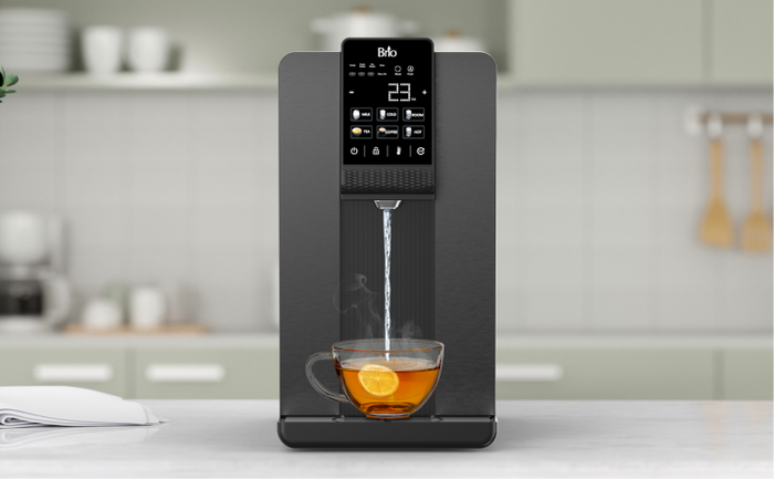 Brio Hydroport black Q20 countertop water dispenser with digital controls, dispensing hot water in a tea cup with lemon in a modern kitchen setting. 