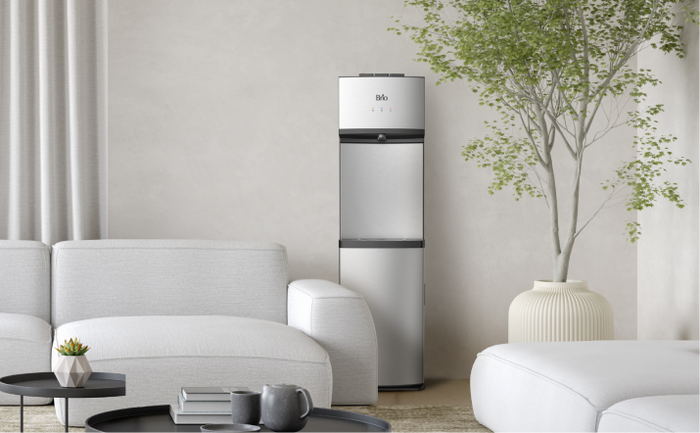 Brio 530 stainless steel bottleless water cooler placed in a cozy living space with light furniture, neutral decor, and a potted tree.