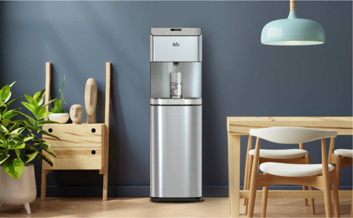 Brio stainless steel bottleless water cooler in a modern dining space with blue walls, light wood furniture, and green plants.
