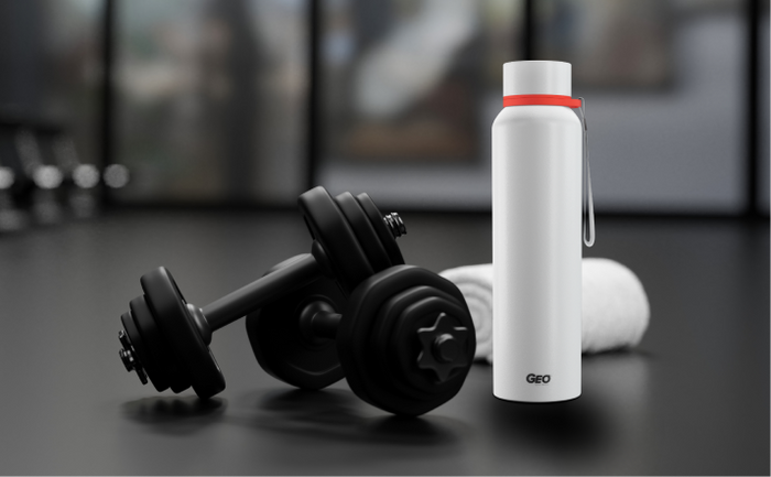 White GEO reusable water bottle placed on a gym floor beside black dumbbells and a rolled towel.