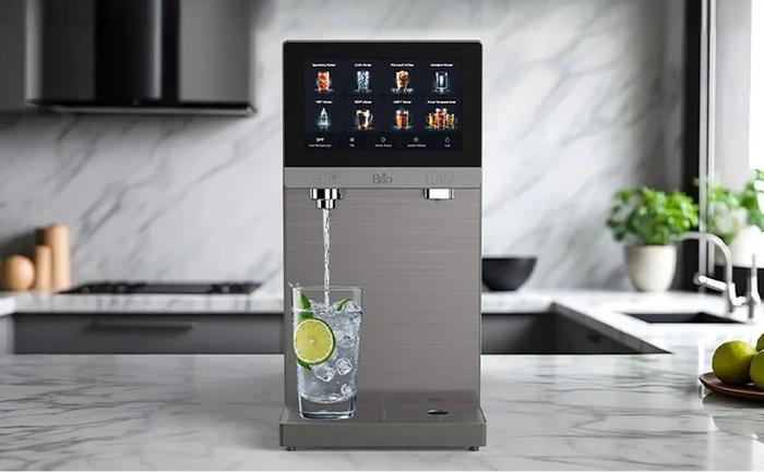 Brio Q60 4-Stage RO Sparkling Countertop Dispenser on a marble countertop with a touchscreen interface showing beverage options, dispensing sparkling water with lime and ice.