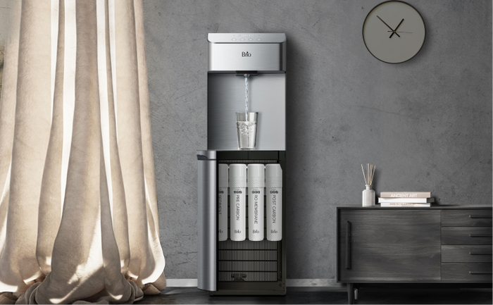 Brio 4-stage reverse osmosis water cooler with built-in reverse osmosis filtration, dispensing water into a glass in a contemporary living room with neutral tones.