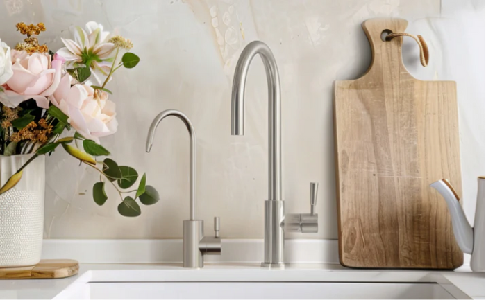 Brio brushed stainless steel kitchen faucet with an undersink reverse osmosis system, placed beside a vase of flowers and a wooden cutting board on a white countertop.