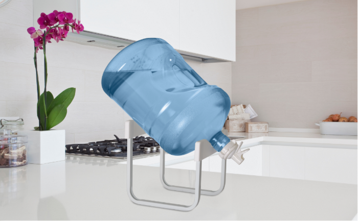 Brio water bottle stand holding a tilted 5-gallon water bottle on a white kitchen countertop with orchid plant decor.
