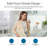 A smiling woman stands in a bright kitchen, holding a glass of water from her Brio Curvy Classic Series Water Faucet-White. Overhead text reads, Safe Food-Grade Design. Three icons below show: lead-free, food-grade, and 304 stainless steel.
