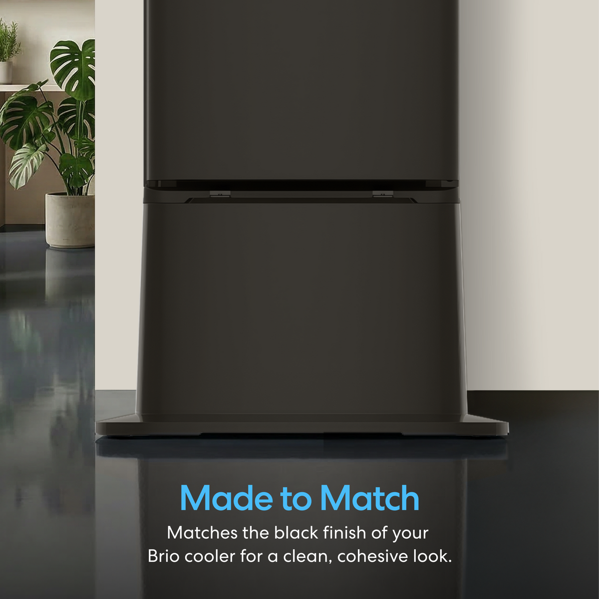 A close-up of the bottom half of a sleek, black Ice Maker + Water Dispenser Cooler Base - 320 Series with a glossy floor and indoor plants. Text reads: Made to Match. Pairs seamlessly with your 320 Series cooler for a clean, cohesive look.