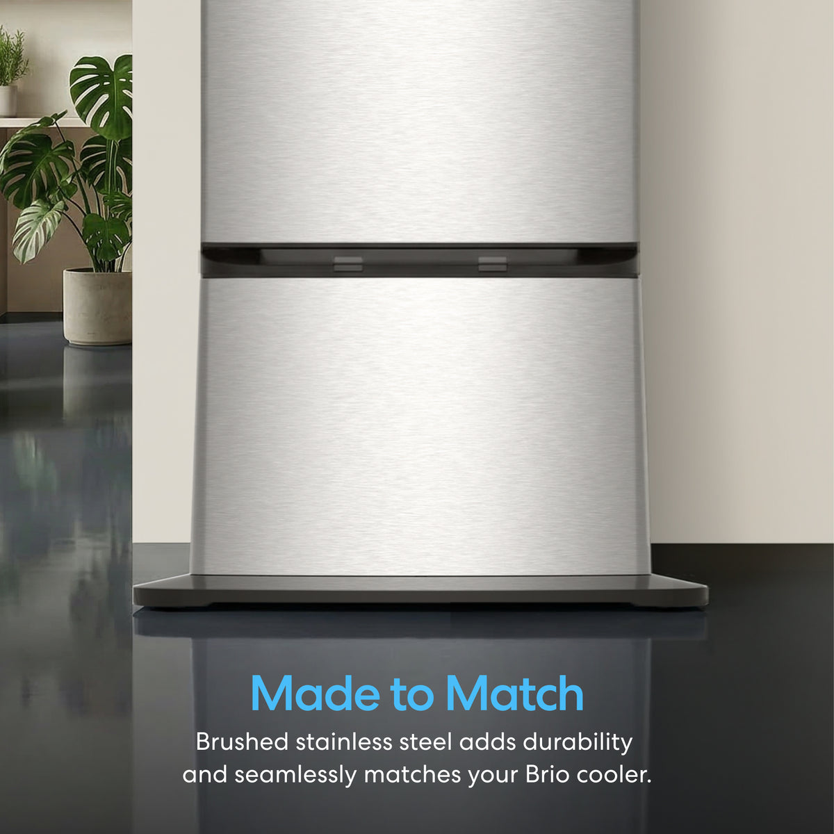 A close-up of a brushed stainless steel Cooler Base for 420 & 520 Series Icemaker Dispensers with a plant in the background. Text reads: Made to Match. Brushed stainless steel adds durability and complements your dispenser.