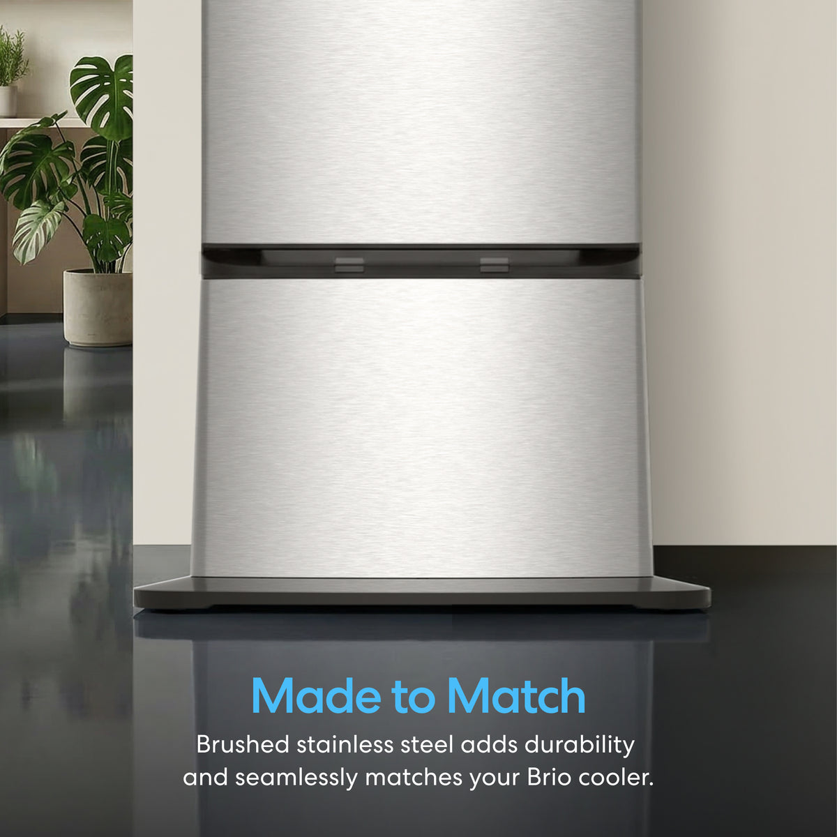 A close-up of the Water Dispenser Cooler Base - 740 Series in brushed stainless steel with "Made to Match" text. Durable steel seamlessly matches Brio 740 Series Water Coolers. Modern interior and plants in background.