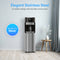A Bottom Load Water Dispenser - Model 420 stands against a light blue wall near a small wooden table topped with a vase of white flowers. Text highlights the dispenser’s elegant, modern design and its ability to elevate any décor.