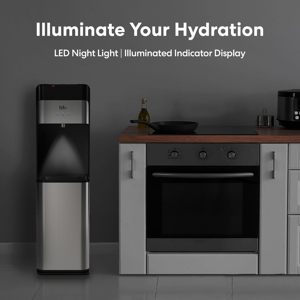 A Bottom Load Water Dispenser - Model 430 with a stainless steel finish and LED night light stands next to a kitchen counter and oven in a modern kitchen. Combining style and convenience, this hot and cold water dispenser features an illuminated indicator display, making it the ideal addition to any home. Text above reads, Illuminate Your Hydration. LED Night Light | Illuminated Indicator Display.