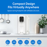 The Brio SIMPL 2-Stage Countertop Water Dispenser with a digital display sits on a kitchen counter by utensils, a plant, and a cup being filled. Features include a 2.5L refillable tank and suitability for kitchens or offices.