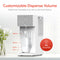 The SIMPL W3 Countertop 2-in-1 Mineralization Water Filter Dispenser fills a glass pitcher with filtered water. The display features presets: 5, 8.5, 16.9, and 33.8 oz. A red circle states No Overfills. White tiles and flowers are in the background.