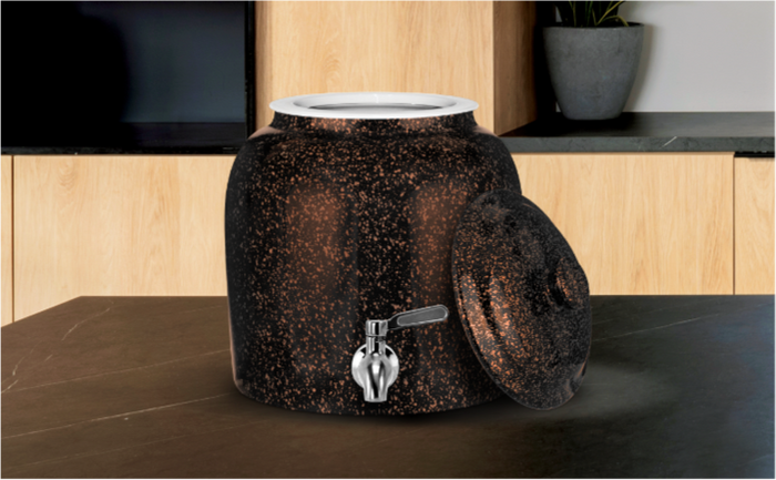 Black speckled ceramic water dispenser with silver spigot and matching lid resting on the side, placed on a dark countertop in a modern kitchen with wooden cabinets and a potted plant in the background.
