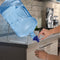 A person uses the 48MM Dark Blue Screw Top Valve Display Package on a water jug with a spout on a metal stand to fill a glass in a modern kitchen.