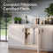 The 26″ Premium Under Sink Filter PFAS-Reduction System mounted on a white kitchen cabinet door, shown in a bright modern kitchen with the text 'Compact Filtration. Certified Clean.
