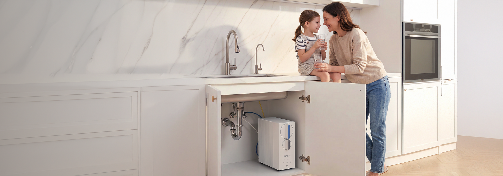 Bright modern kitchen with a mother and young daughter smiling and holding glasses of water by the sink, with a Brio SIMPL RO undersink water filtration system visible inside an open cabinet.