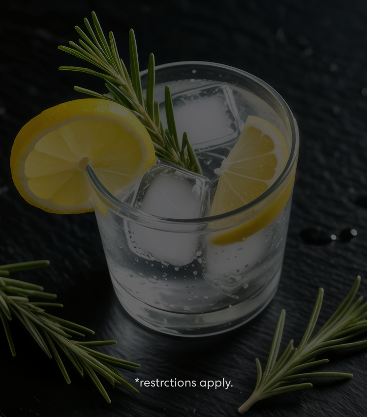 Refreshing glass of sparkling water with ice cubes, lemon slices, and rosemary garnish on a dark textured surface, with small text reading “restrictions apply.”