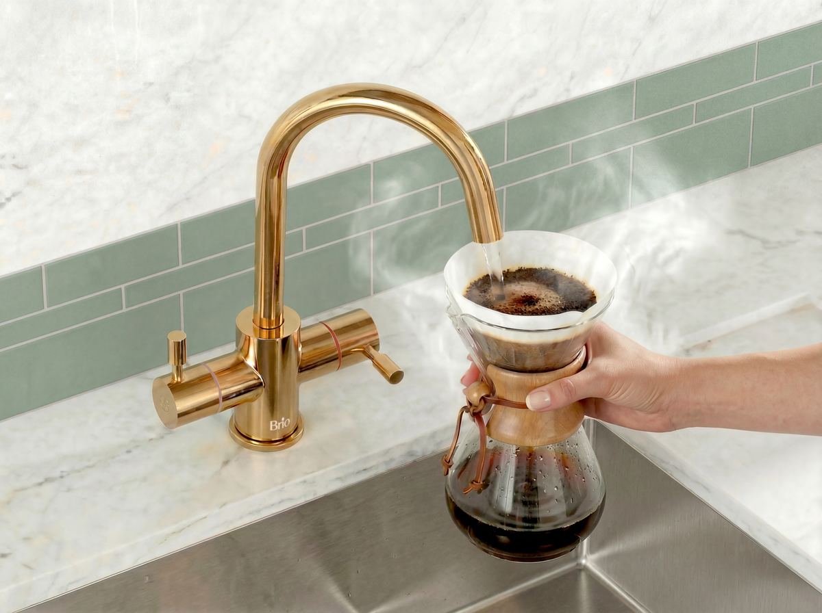 Modern kitchen with a gold faucet dispensing steaming hot water into a pour-over coffee maker, showcasing the Brio 3-Stage Undersink Filtration System with instant hot water for convenient brewing.