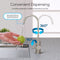 A hand rinses a green apple under the Modern Series Water Faucet-31mm Brushed Nickel, featuring dual spouts, 360° rotation, a 90° handle, and a splash-free water stream on a gray countertop.